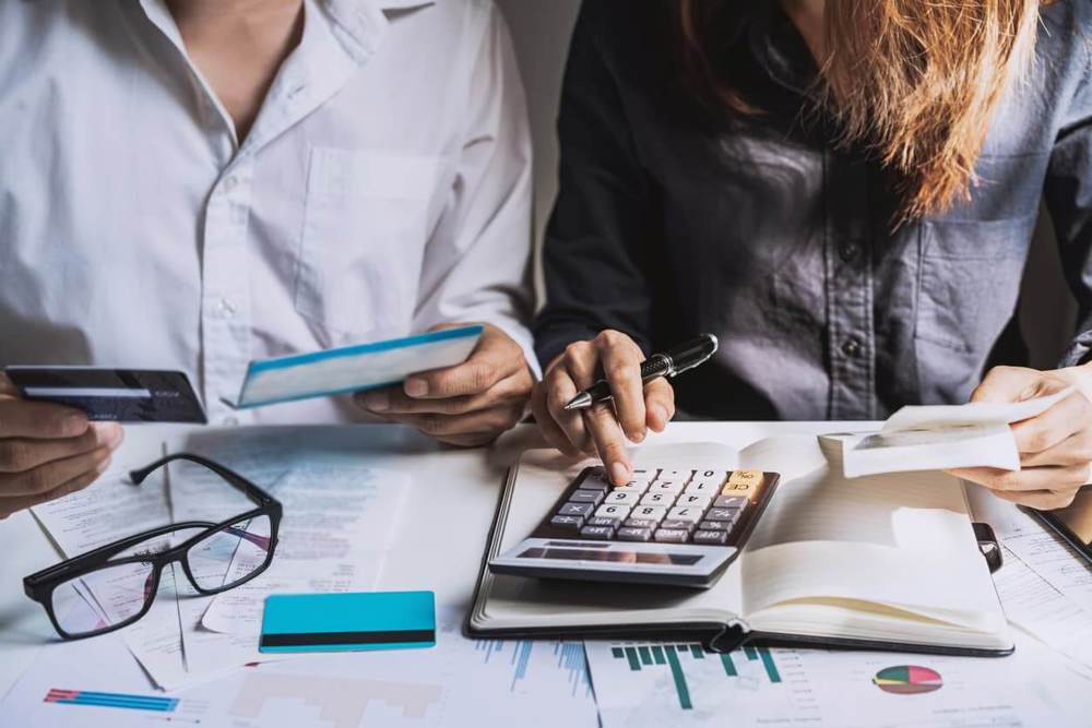 Two people sat at desk using a calulator and a holding bank card