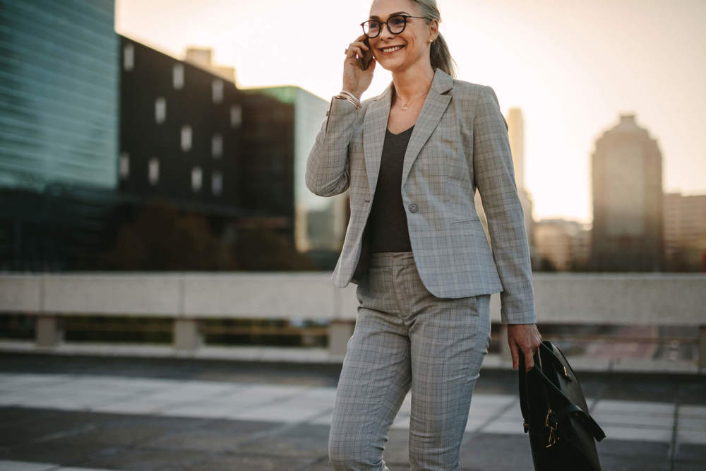Woman in grey suit walking while on the phone and holding a briefcase