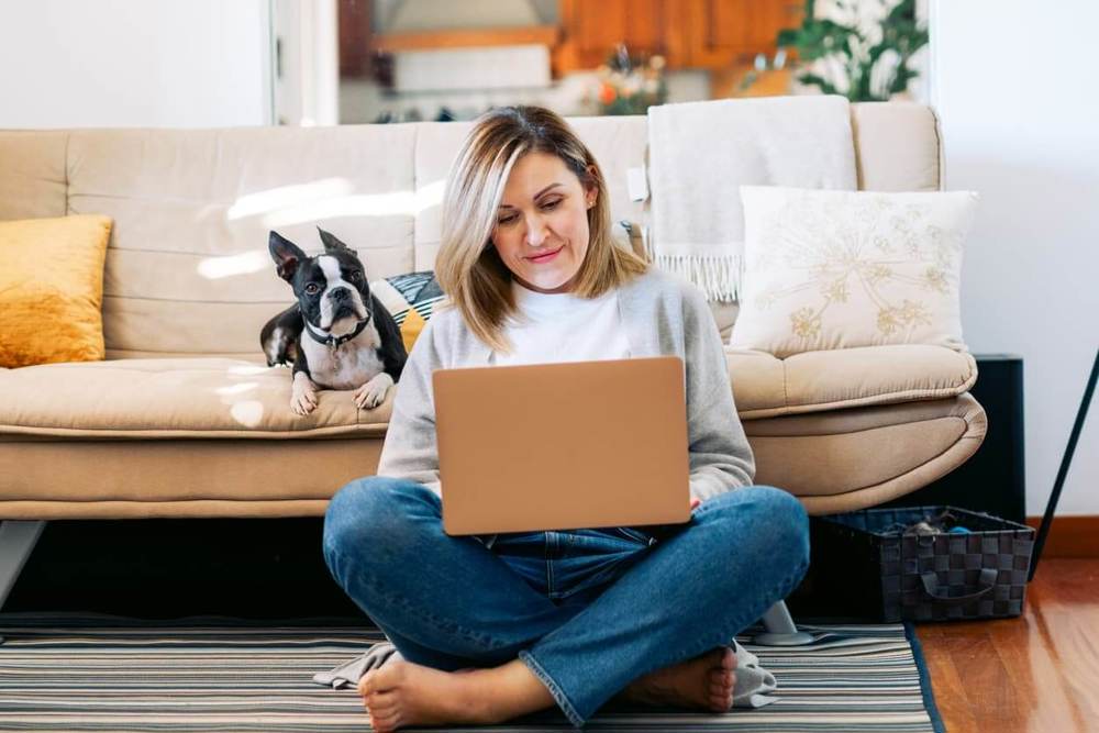 Woman sat on the floor with laptop on knees smiling
