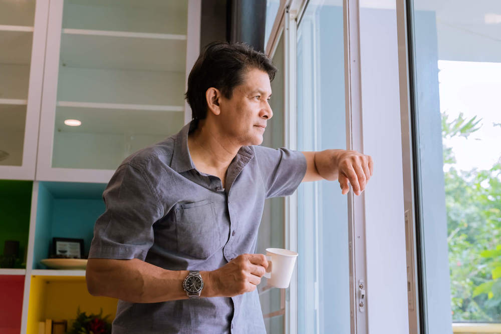 Man holding cup while staring out of a window