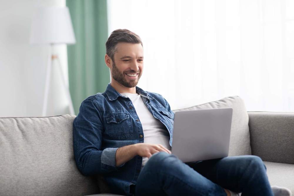 Man sat on couch smiling at laptop