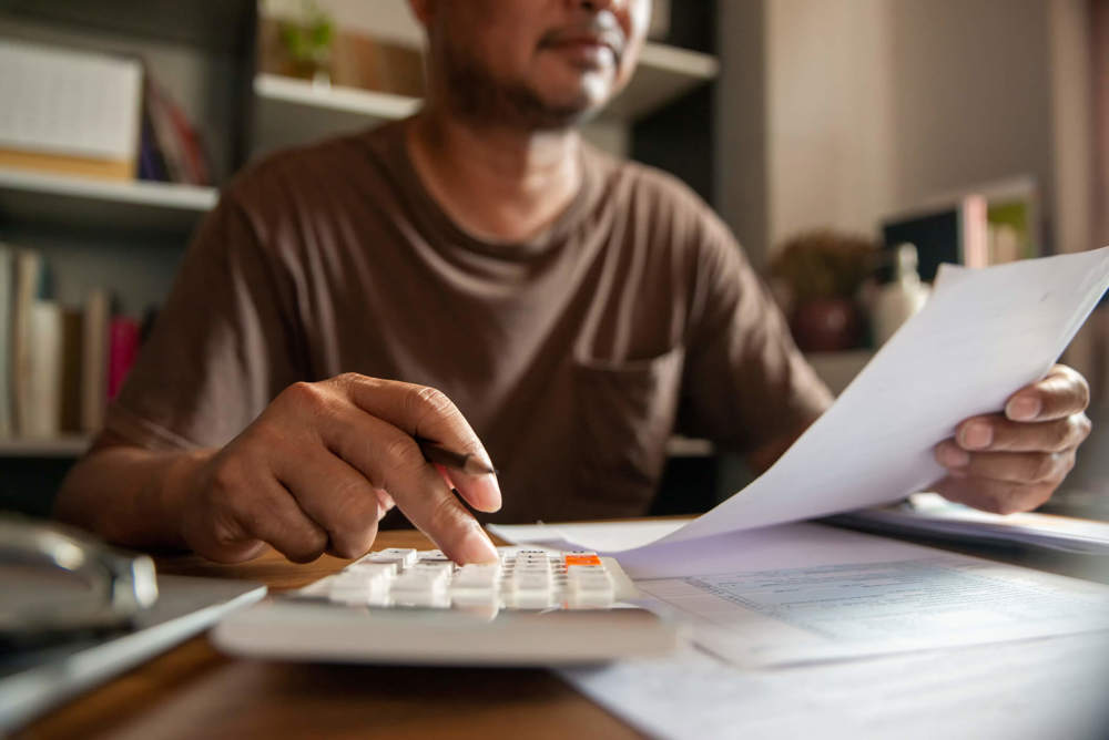 Man sat at desk looking at paper while touching a calculator